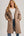 Woman wearing a long quilted brown coat on a plain background