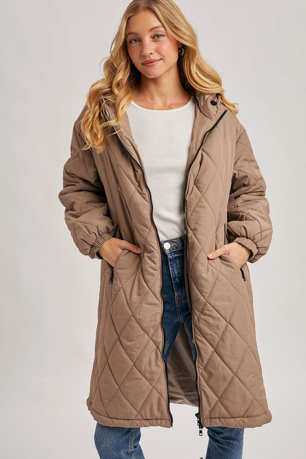 Woman wearing a long quilted brown coat on a plain background