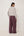 A woman is shown from the back wearing a gray and white horizontally striped long-sleeve crop top and wide-leg mauve purple trousers, standing against a plain white wall.