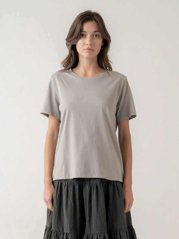 Woman wearing a plain gray t-shirt and dark skirt against a white background