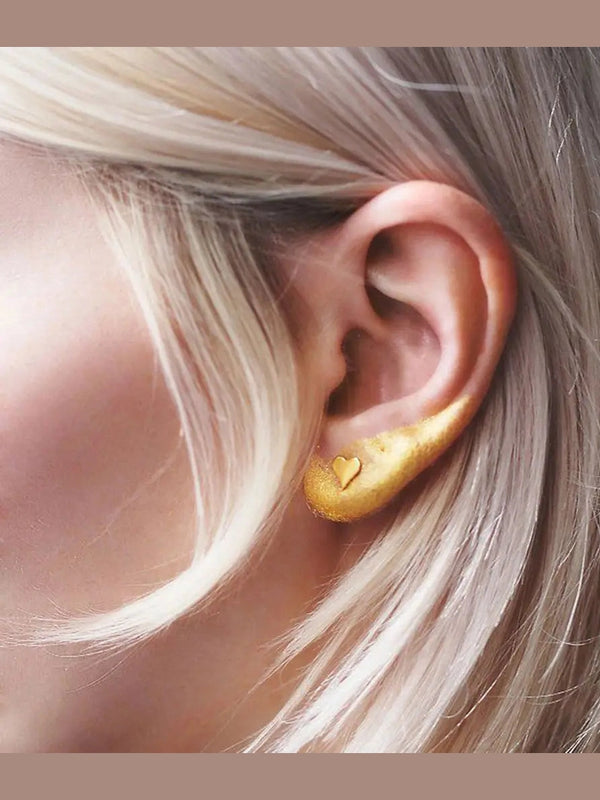 Gold heart-shaped earring worn by a person with blonde hair.