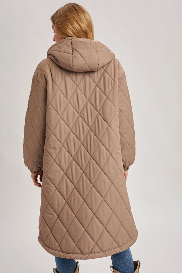 Person wearing a long quilted beige coat on a plain background