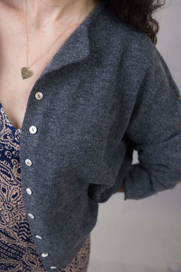 Person wearing a dark gray cardigan with button details on a neutral background