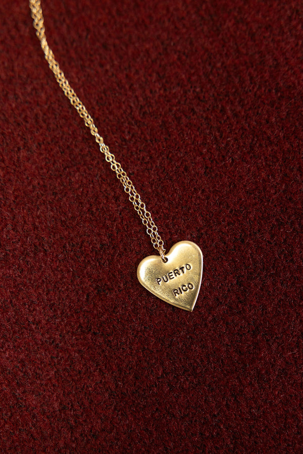 Gold heart-shaped pendant necklace with 'Puerto Rico' engraving on a red background