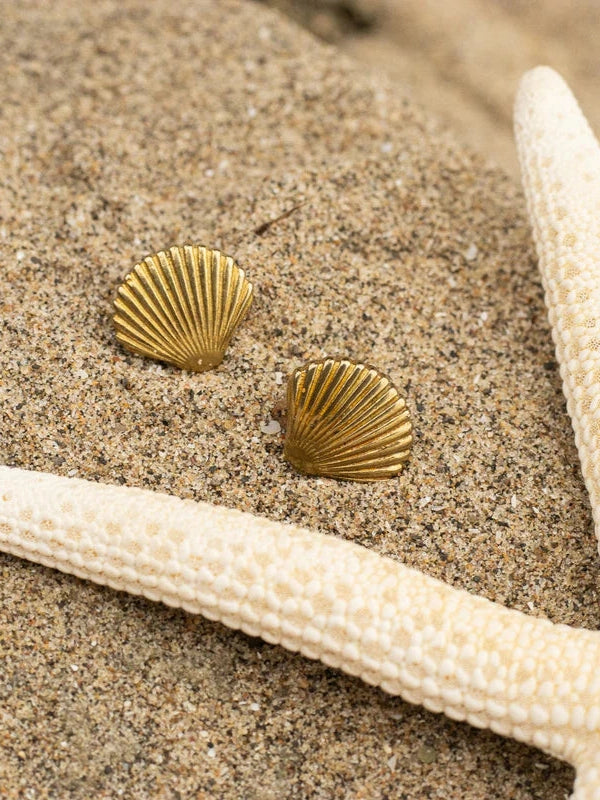 Gold shell-shaped earrings on sand with starfish