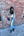 Woman in a beige coat standing against a brick wall, holding an ice cream cone.