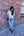 Woman standing against a brick wall holding a drink, wearing sunglasses and casual clothing.