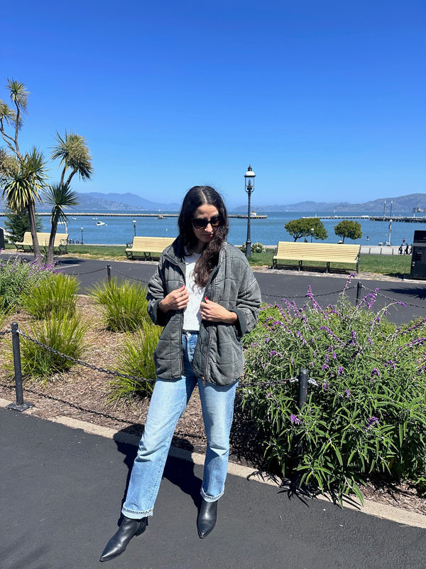 Person standing outdoors with a clear blue sky and plants in the background