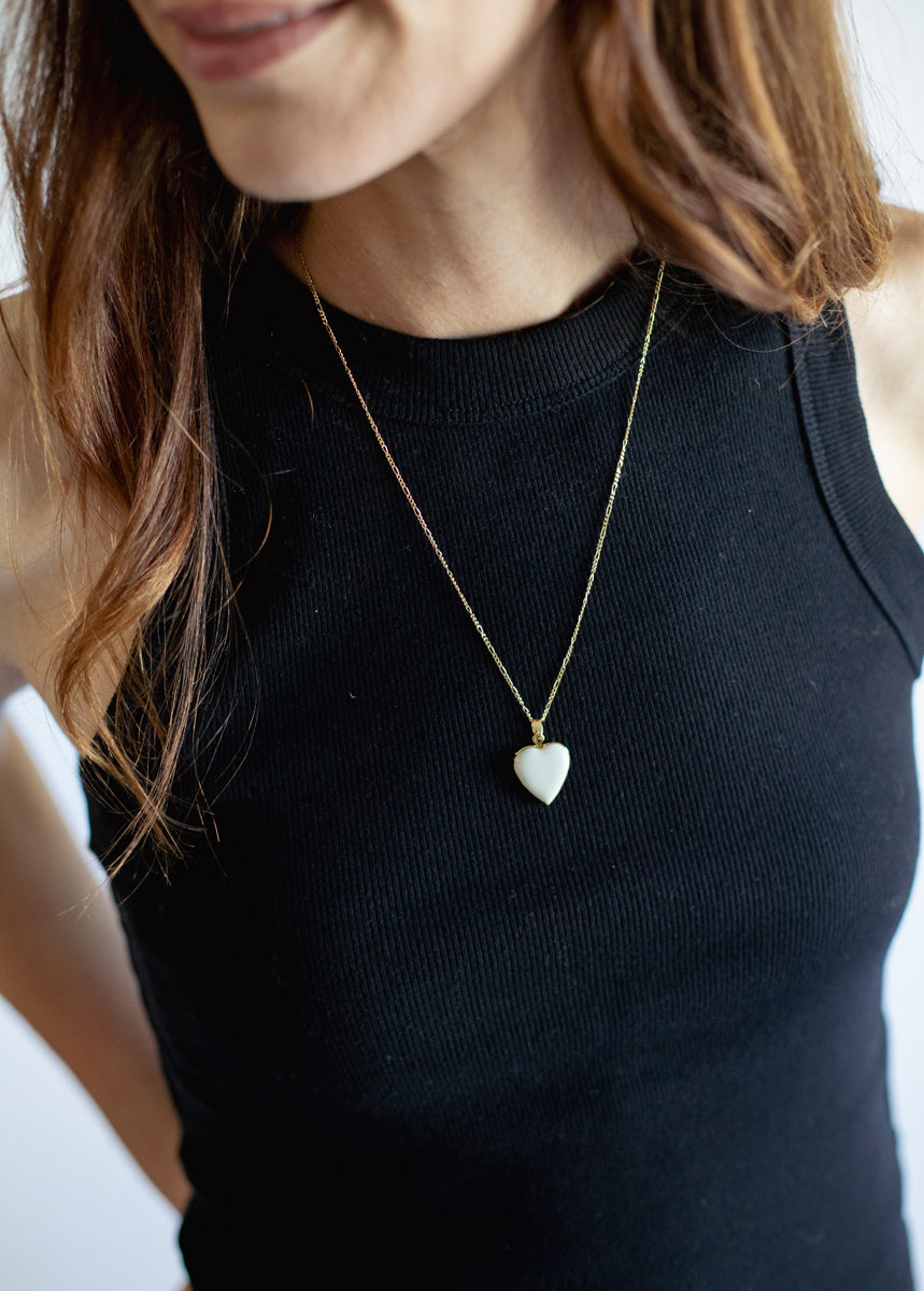 Person wearing a black top with a gold necklace featuring a heart-shaped pendant.