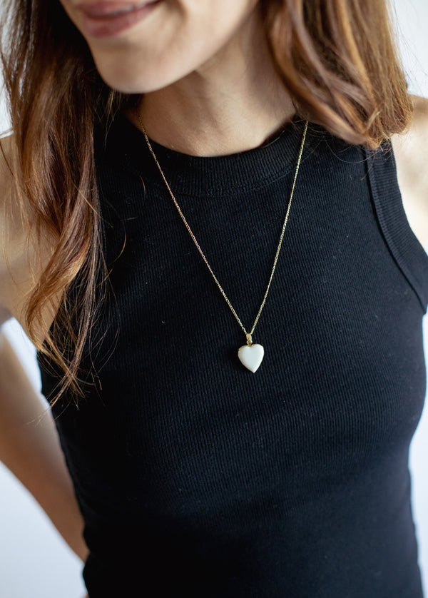 Person wearing a black top with a gold necklace featuring a heart-shaped pendant.