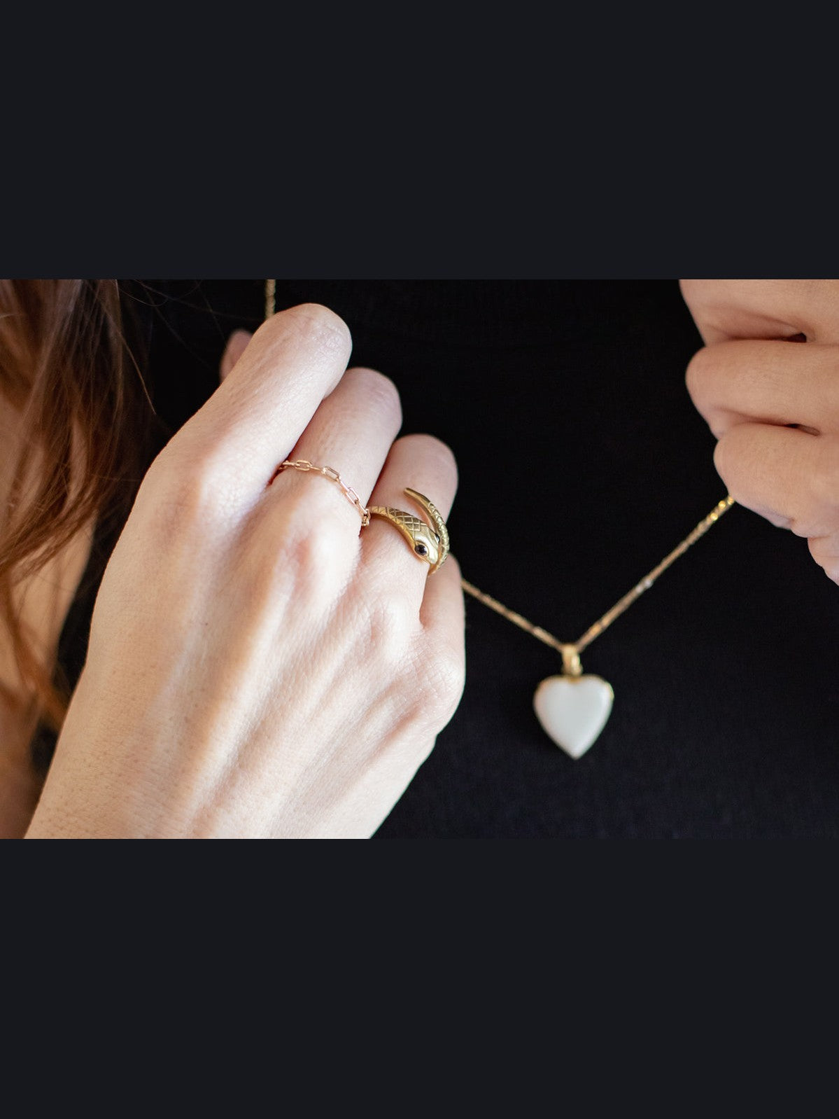 Heart-shaped pendant necklace being held by a hand with gold rings on a dark background