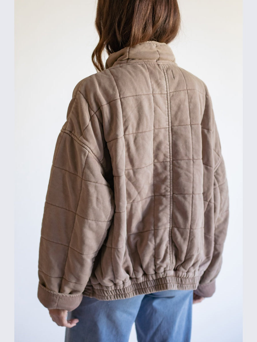 Person wearing a quilted brown jacket against a white background