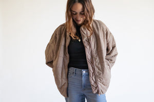 Woman wearing a blush color jacket over a black top and blue jeans on a white background