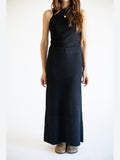 Person wearing a black sleeveless top and long black pleated skirt on a white background