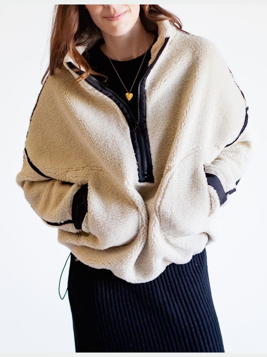 Person wearing a beige fleece jacket with black accents on a white background