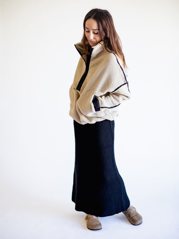 Woman wearing a beige and black jacket with a navy skirt on a white background
