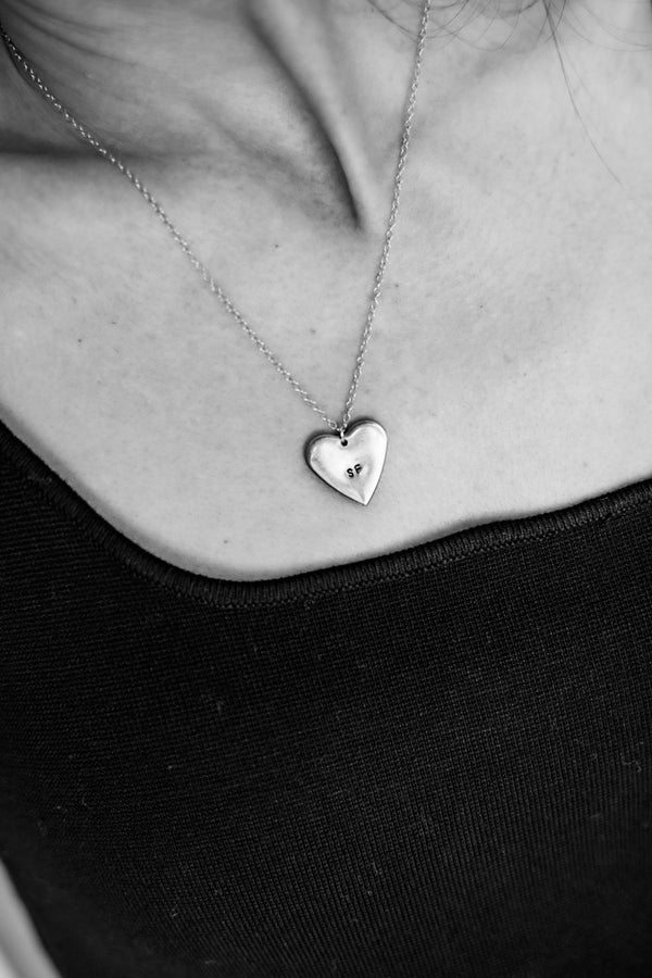 Silver heart-shaped necklace on a person wearing a black top.