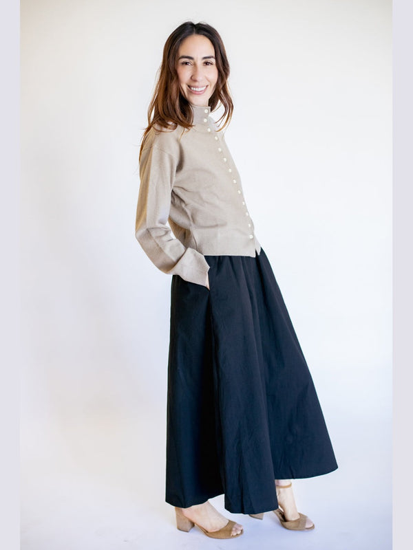 Woman wearing a beige sweater and navy skirt on a white background