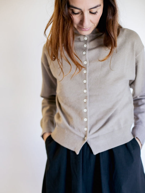 Woman wearing a light gray cardigan with a plain background