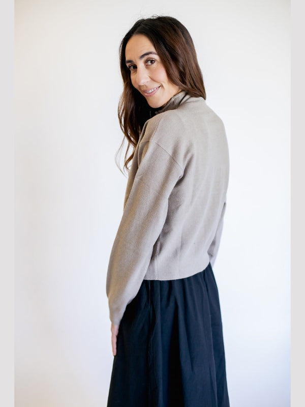 Woman wearing a light gray sweater and dark blue skirt against a white background