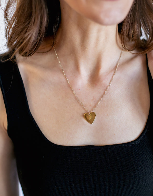 Gold heart-shaped necklace worn by a person with a black top