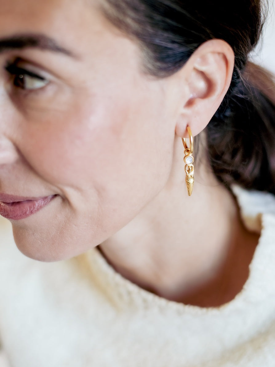 Close-up of a woman wearing gold hoop earrings with a blurred background