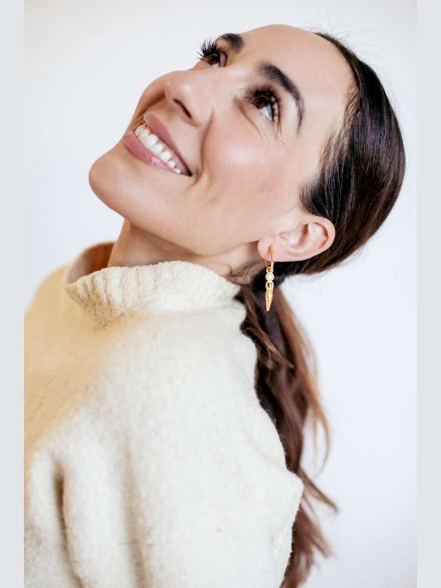 Woman wearing a beige sweater and gold earrings against a white background