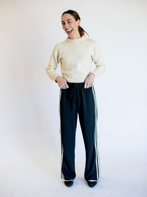 Woman wearing a cream sweater and black pants with white stripes on a white background
