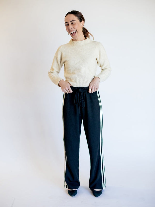 Woman wearing a cream sweater and black pants with white stripes on a white background