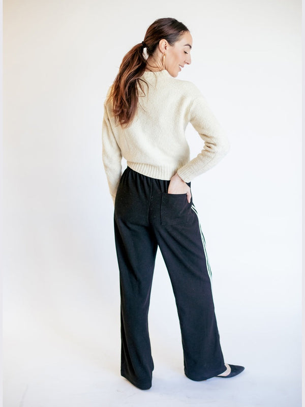Woman wearing a cream sweater and black pants against a white background