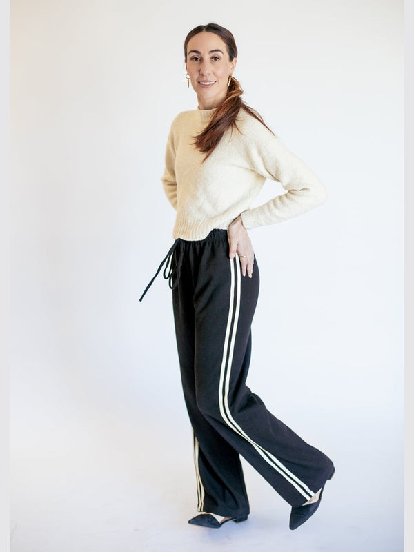 Woman wearing a beige sweater and black pants with white stripes on a white background
