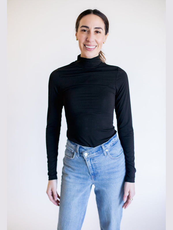 Person wearing a black turtleneck and light blue jeans against a white background