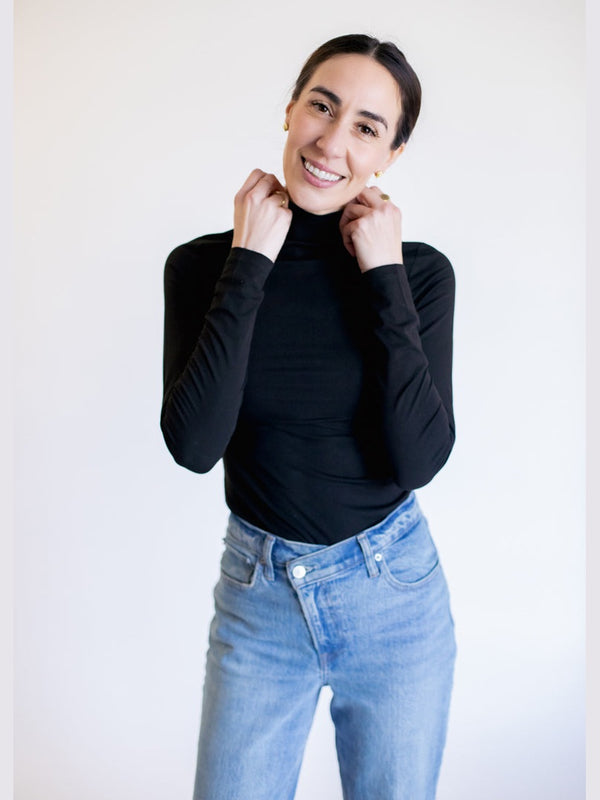 Person wearing a black turtleneck and light blue jeans against a white background