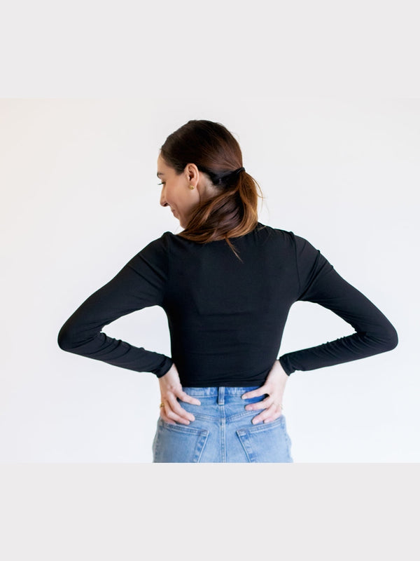 Woman wearing a black long-sleeve top and blue jeans against a white background