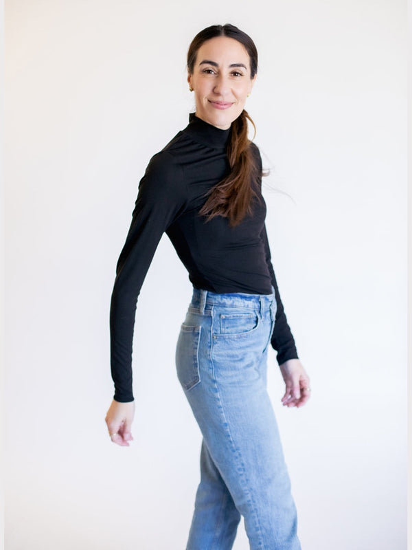 Woman wearing a black long-sleeve top and blue jeans on a white background