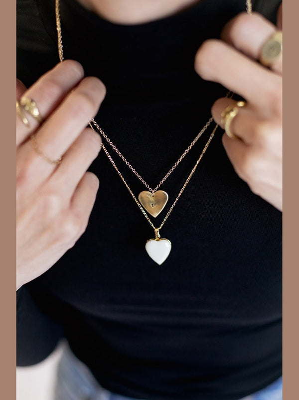 Person wearing a black top with layered gold and heart-shaped pendants on a necklace.
