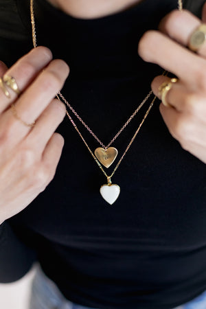 Person wearing a black shirt with gold necklaces featuring heart-shaped pendants.