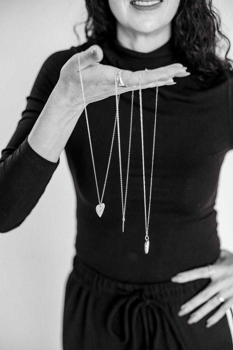 Person holding three necklaces with heart pendants against a plain background