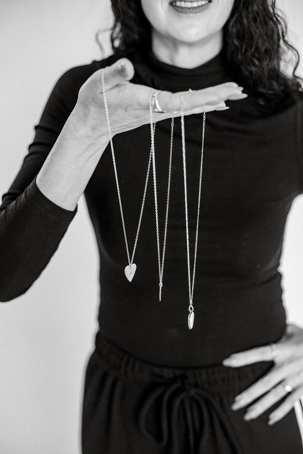Person holding three necklaces with heart pendants against a plain background