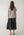 Woman wearing a light gray t-shirt and dark gray tiered skirt on a white background