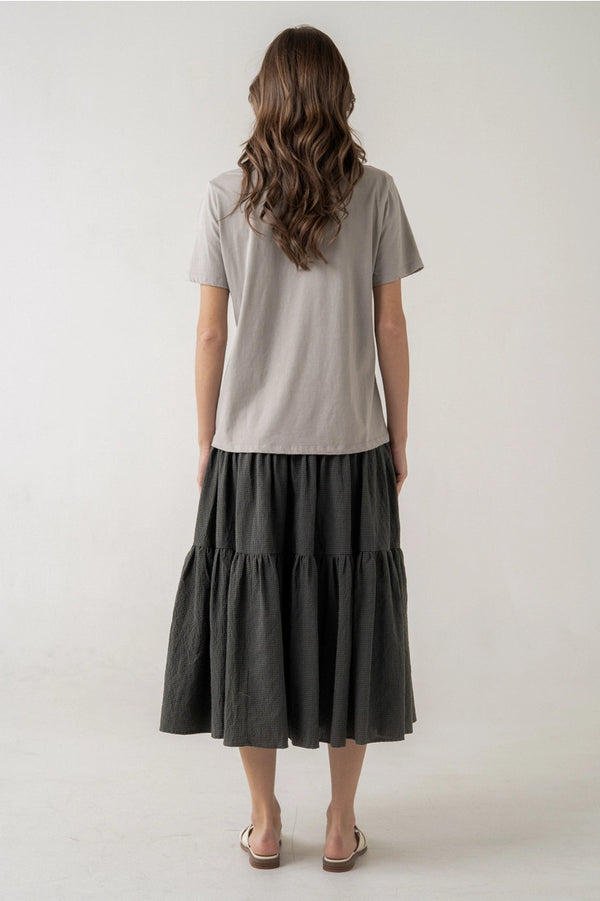 Woman wearing a light gray t-shirt and dark gray tiered skirt on a white background