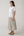 A woman modeling a white short-sleeve crewneck t-shirt and a tiered midi skirt with vertical beige and black stripes, paired with tan slide sandals, against a plain light gray studio background.