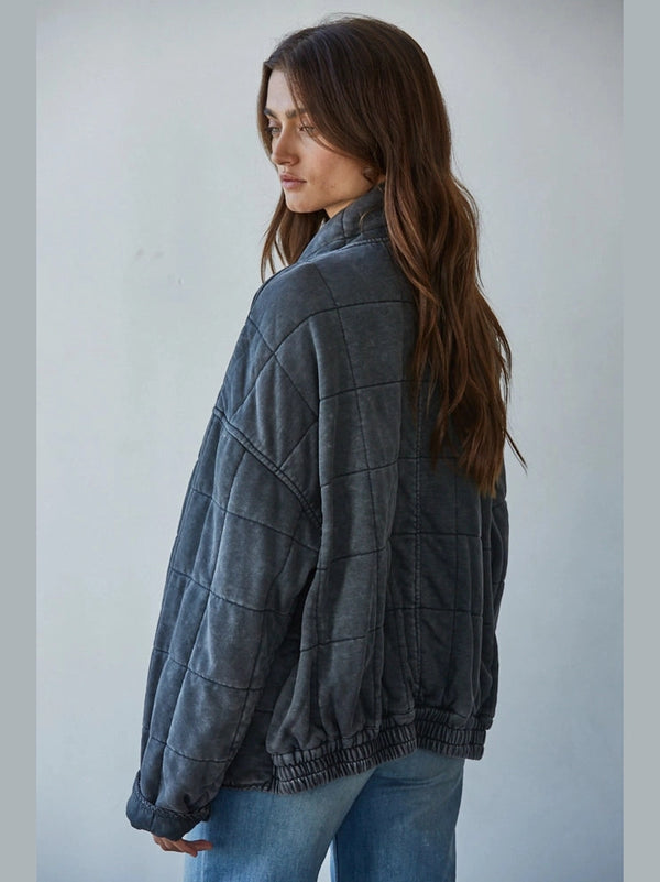Woman wearing a dark gray jacket and blue jeans against a plain background