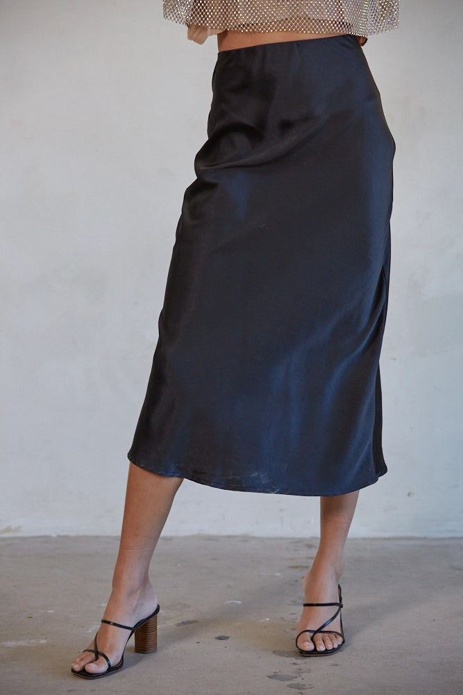 Person wearing a black satin skirt against a plain background