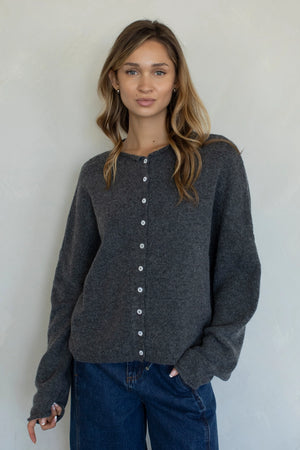 Woman wearing a dark gray cardigan with white buttons against a plain background