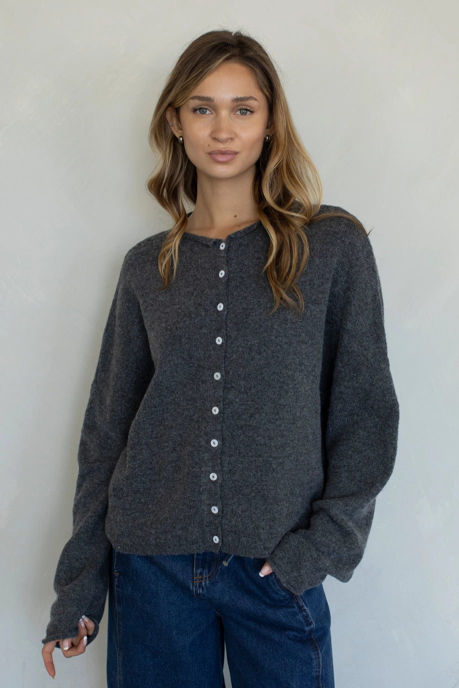 Woman wearing a dark gray cardigan with white buttons against a plain background
