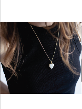 Person wearing a necklace with a heart-shaped pendant on a plain background