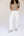 A model wearing white straight-leg jeans, a beige knit sweater, and beige slip-on shoes, standing against a plain light background.