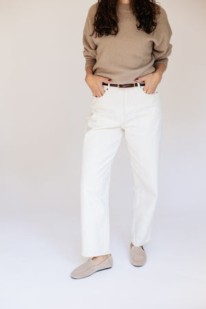 A model wearing white straight-leg jeans, a beige knit sweater, and beige slip-on shoes, standing against a plain light background.