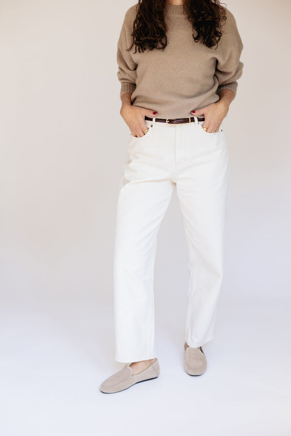 A model wearing white straight-leg jeans, a beige knit sweater, and beige slip-on shoes, standing against a plain light background.